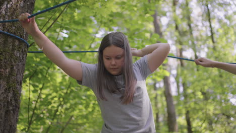Active-child-fearlessly-climbs-the-ropes-between-the-trees.-Girl-in-an-adventure-park-are-pass-obstacles-on-the-rope-road.-children-camp-summer-camp